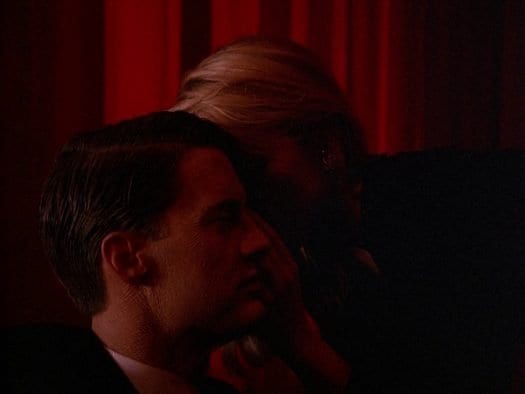 Laura Palmer leans in to whisper something to Dale Cooper. Her face is covered by his profile.