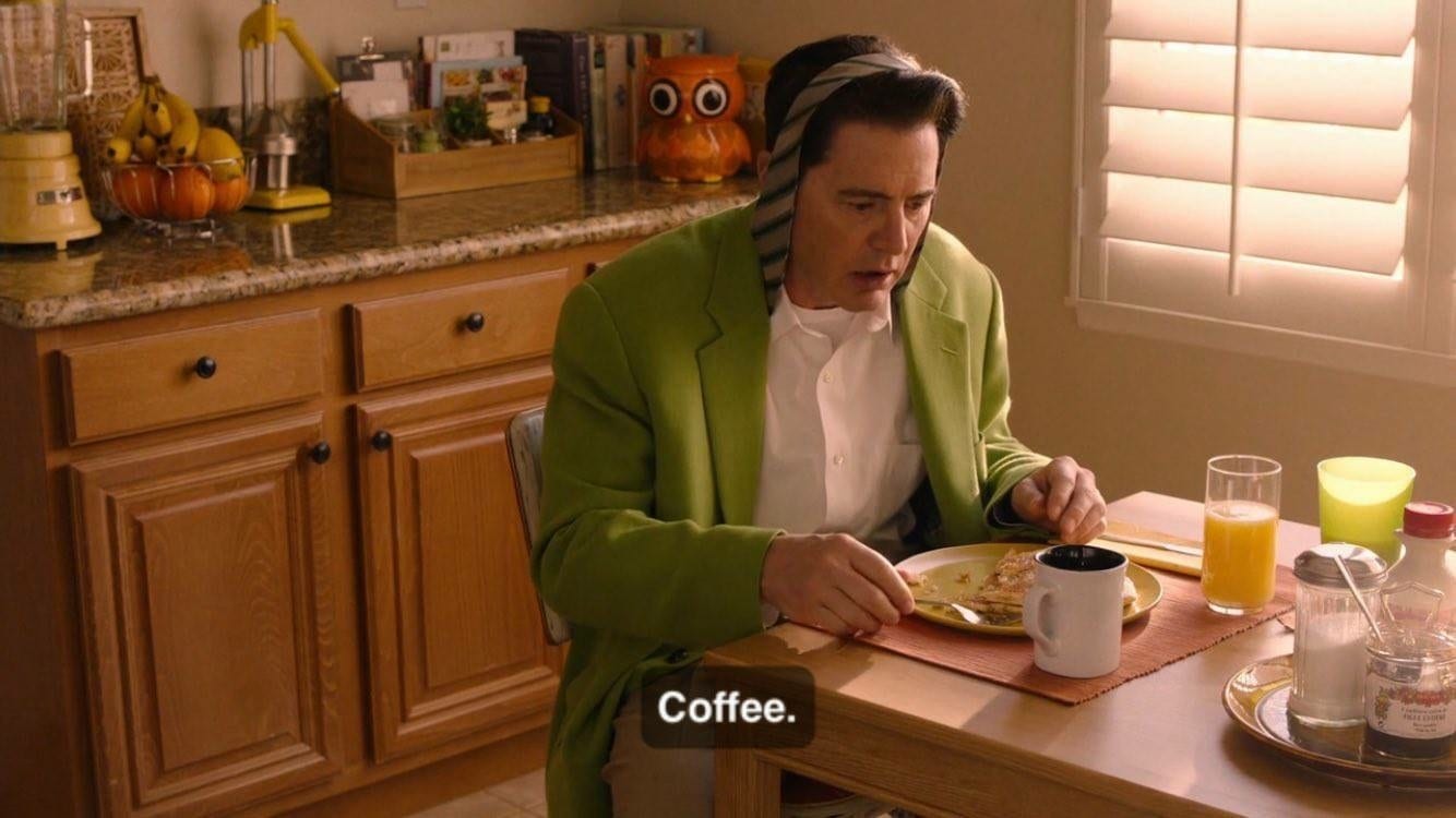 Cooper sits at breakfast table with his tie wrapped over his head and says 'coffee'