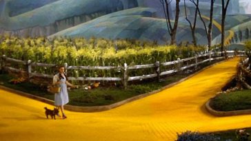 Dorothy and Toto walking down the yellow brick road, approaching a crossroads in the path.