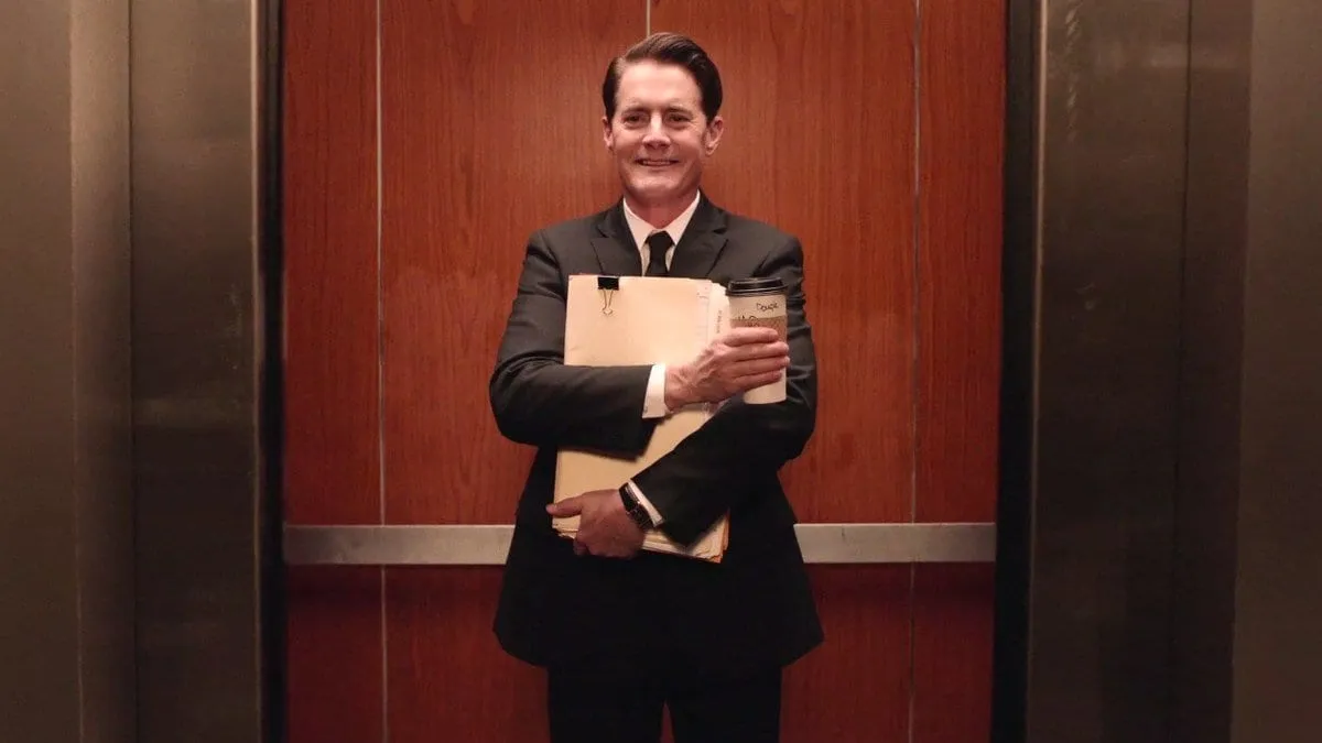 dougie cooper smiles with his coffee in his office elevator