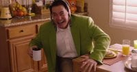 Dougie Jones after spitting out coffee and saying "Hi!" He wears a green coat, his tie is tied around his head, and he leans forward holding his coffee cup.