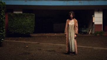 a strange androgynous person wearing a nightgown and robe outside a motel