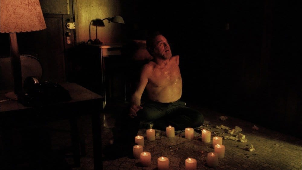 MIKE chants out in a dark room with a circle of candles