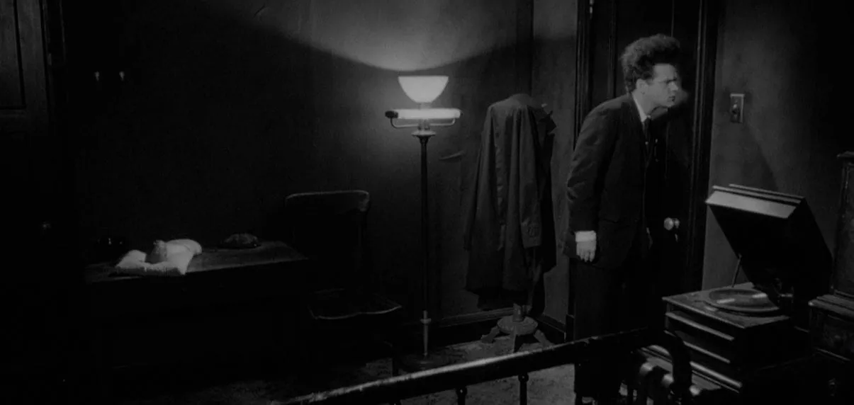 Henry in Eraserhead next to a record player, listening at the door