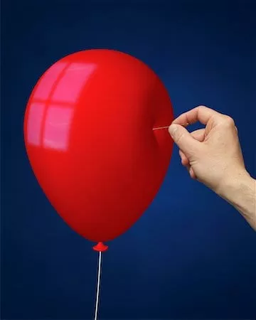 a red balloon with a hand about to stick a pin in it