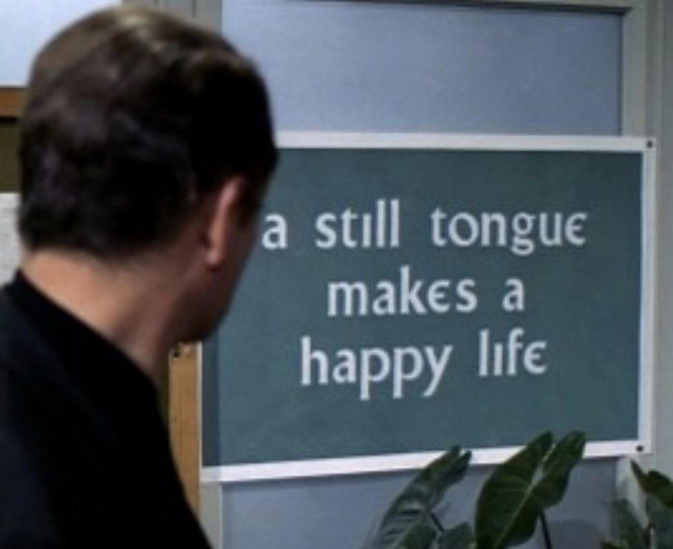 The prisoner reads a sign that says A Still Tongue Makes a Happy Life