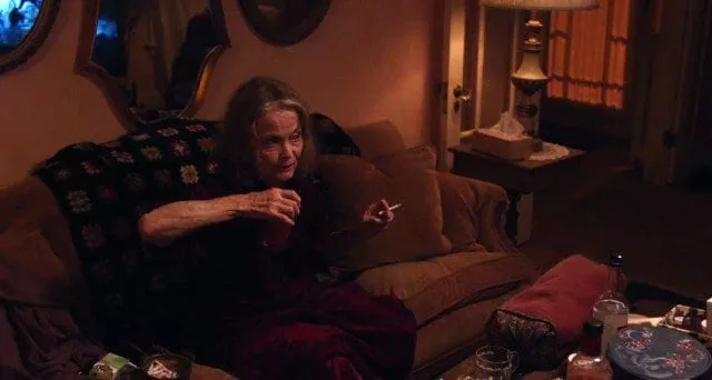 Sarah Palmer sits on her sofa smoking and drinking a Bloody Mary