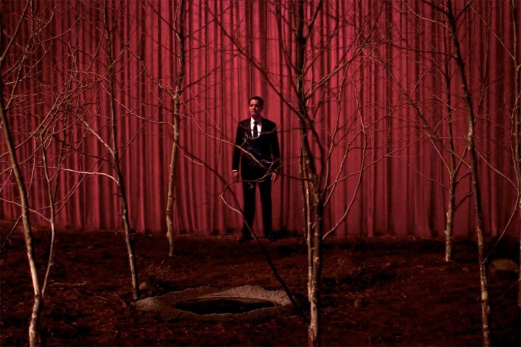 Dale Cooper leaves the Black Lodge through red curtains and stands at a circle of sycamores