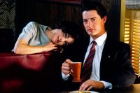 audrey horne rests her head on dale coopers shoulder while he drinks coffee in a booth