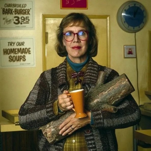 the log lady smiles with a cup of coffee and her log in her arms