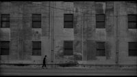 Ronnie Rocket walks past a huge grey building