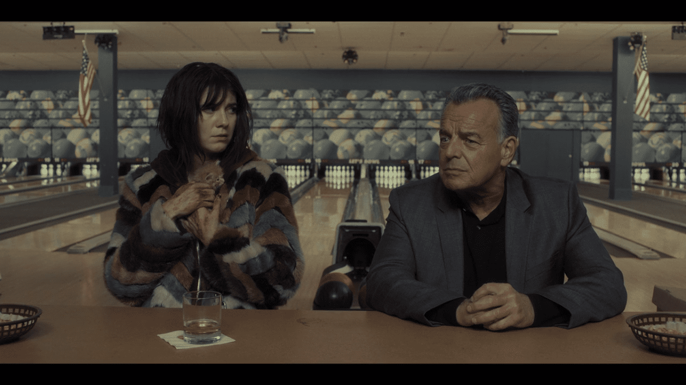 Ray Wise sitting at a bowling alley bar next to a woman holding a kitten