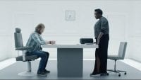 Cooper sits at a white table as he prepares to play a game for Katie in Black Mirror "Playtest"