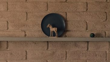 a blue plate against a white wall with a white horse figurine