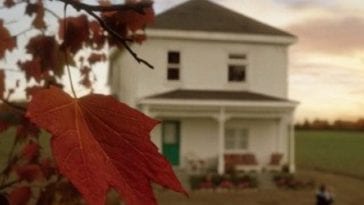 a red maple leaf with a house blurred in the distance