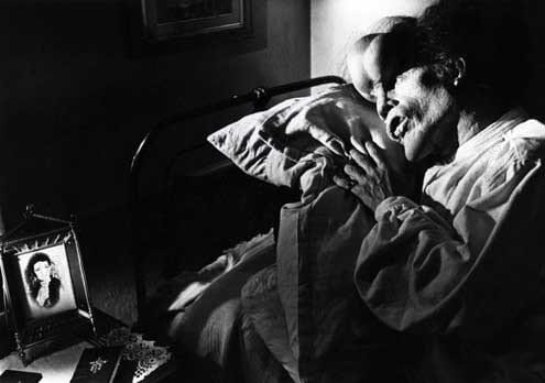 the Elephant man lies on a pillow looking at a photograph of a woman