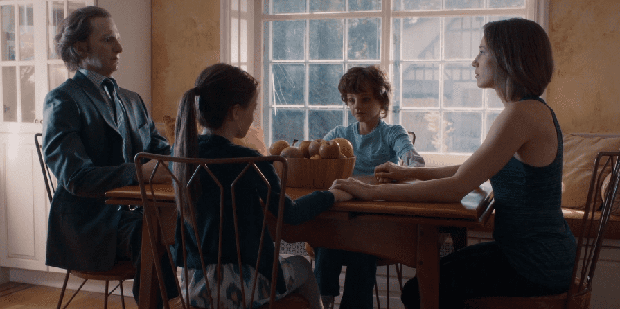 Nora sits at her table with Loved Ones replicas of her family