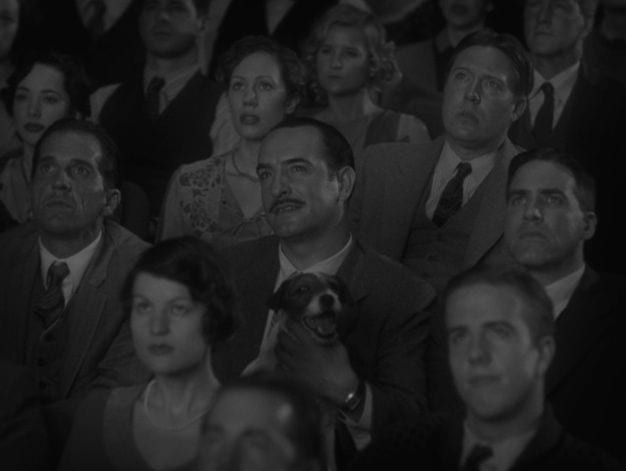 Jean Dujardin as George Valentin with Uggie the dog on his lap in a theatre audience in The Artist