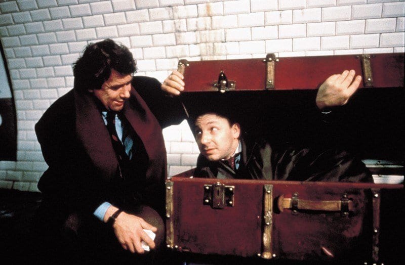 Zbigniew Zamachowski as Karol Karol with a man inside a suitcase