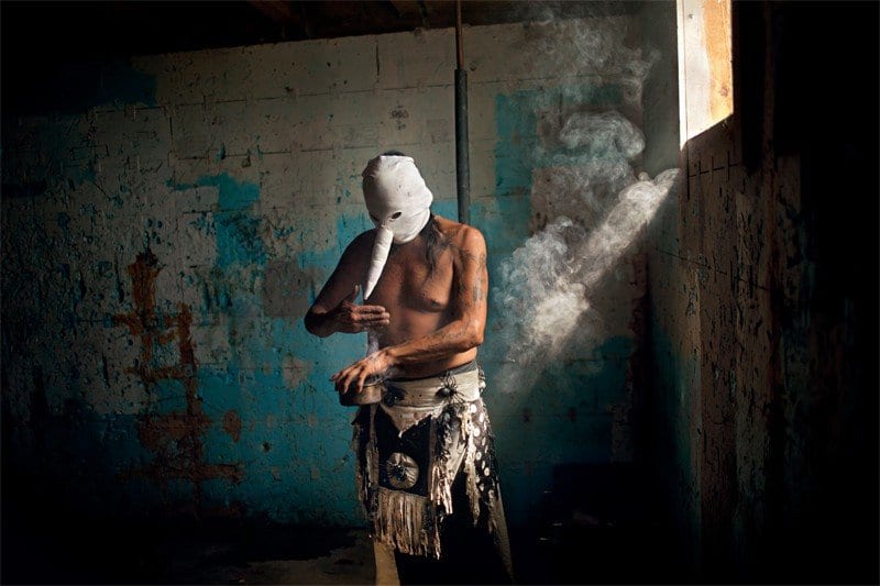 A Heyokah wears a white mask with protruding nose while making a potion