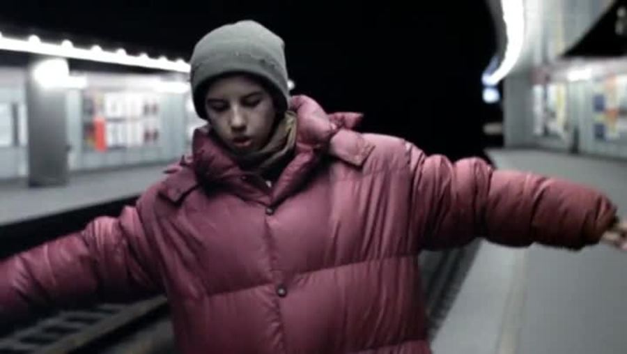 a boy in a red coat walks along an underground train track cautiously