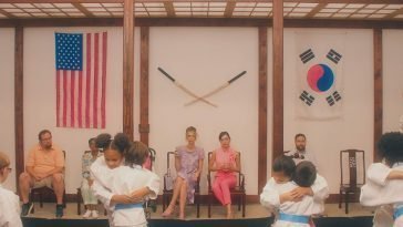 Lisa (left) and Jill (right) sit next to each other while their are in a karate class. There are children hugging in the foreground.