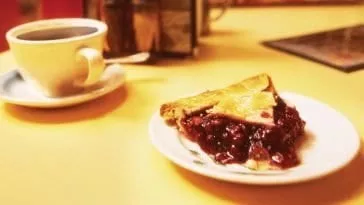 a cup of coffee and a slice of cherry pie on a counter