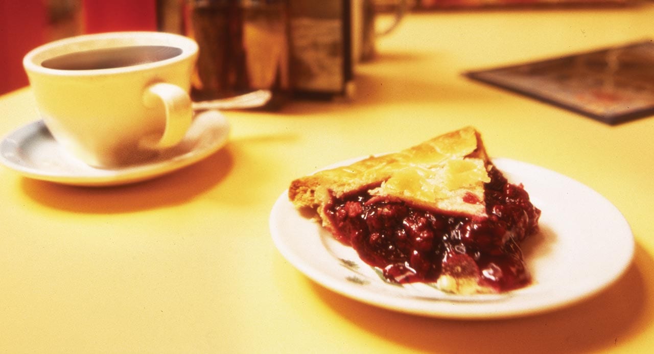 a cup of coffee and a slice of cherry pie on a counter