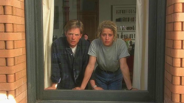 A man and a woman look out of a window with confused looks on their faces