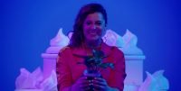 Rebecca (Rachel Bloom) holds a plant with a forced smile on her face