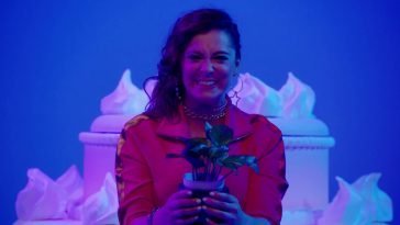 Rebecca (Rachel Bloom) holds a plant with a forced smile on her face