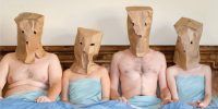 Four people in bed with paper bags over their heads in Baghead.
