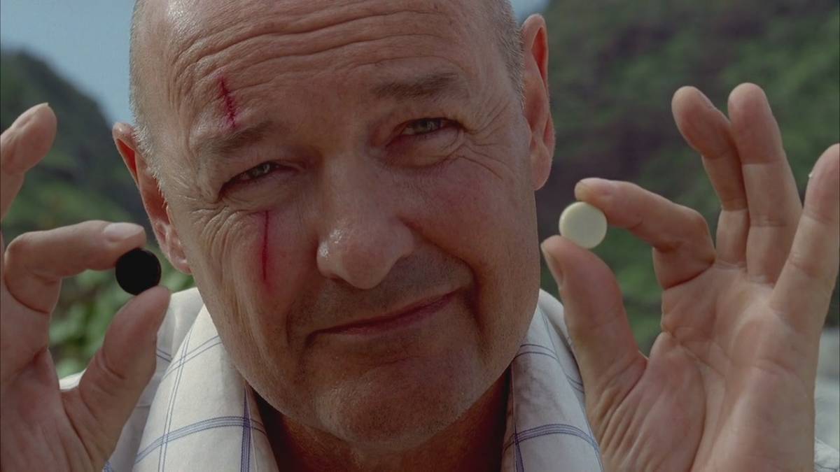 John Locke holds up one black stone and one white stone as he explains Backgammon to Walt