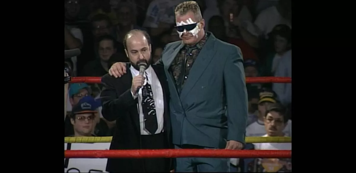 Tod Gordon stands in the ring with a bandaged Sandman wearing sunglasses