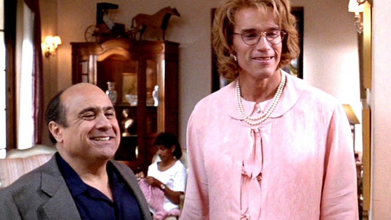 At the maternity retreat, Arnold is in a pink dress and a wig and posing as DeVito's wife. DeVito looks very proud