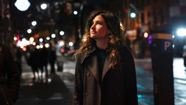 Eve stands on a NYC sidewalk at night looking satisfied