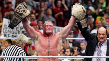Brock Lesnar stands in the ring holding up the WWE Universal title and the Big Gold Belt, as Paul Heyman raises his arm