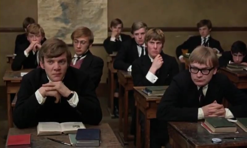 A group of public schoolboys sit at their desk and stare at the front of the classroom