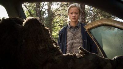 Woman standing at the driver side door of a car that contains a rotted corpse