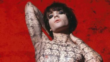 Richey Edwards poses against a red background, his body covered in Marilyn Monroe tattoos