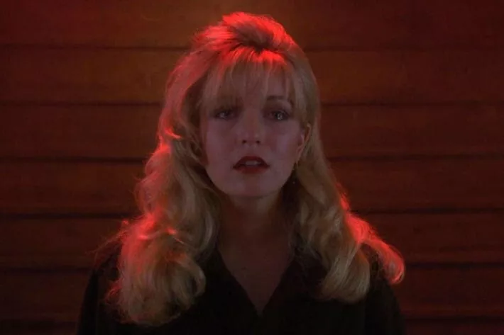 A closeup of Laura Palmer, against a background of a brick wall. Her expression is pained and heartbreaking.