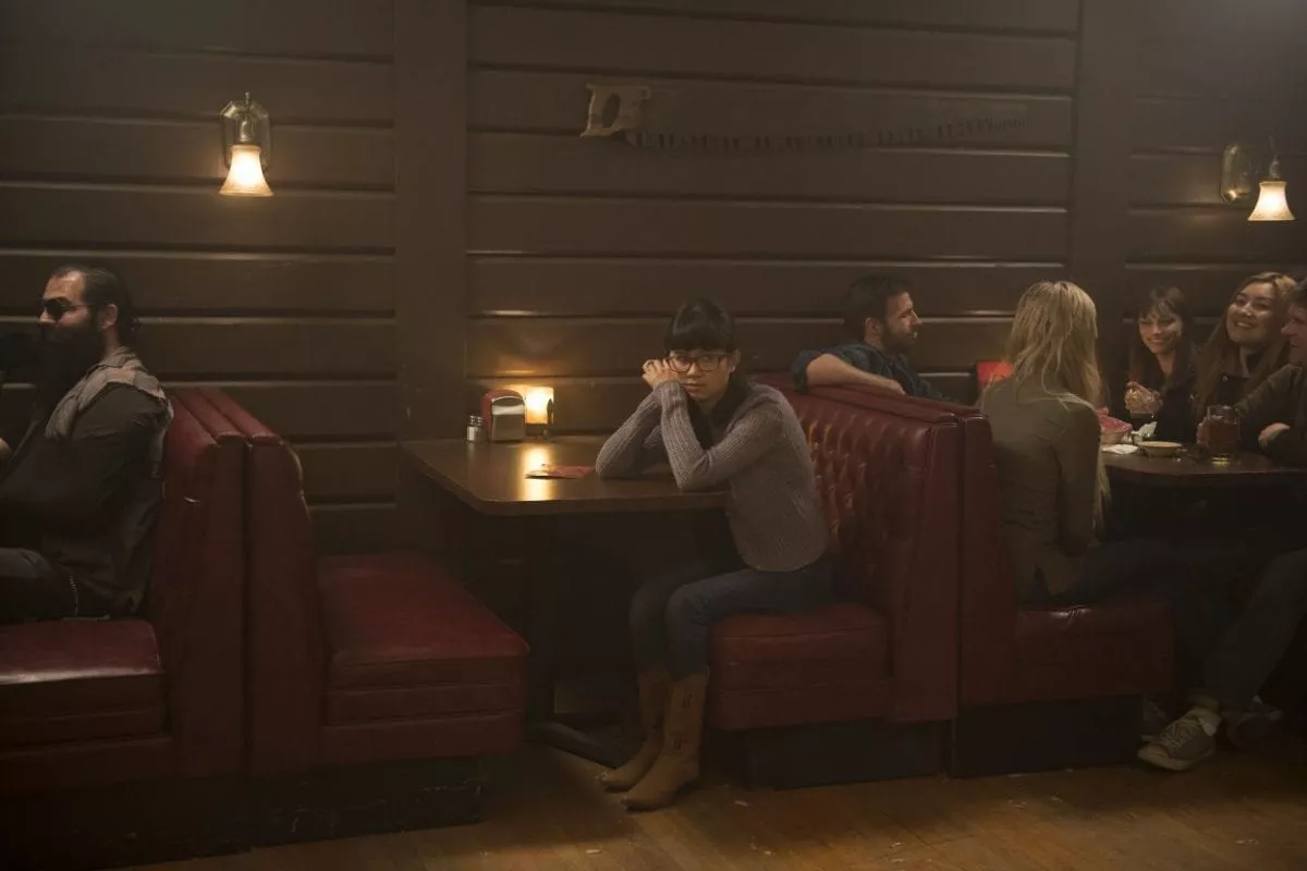 A young girl sits alone at a booth, leaning on her hands, elbows on the table.