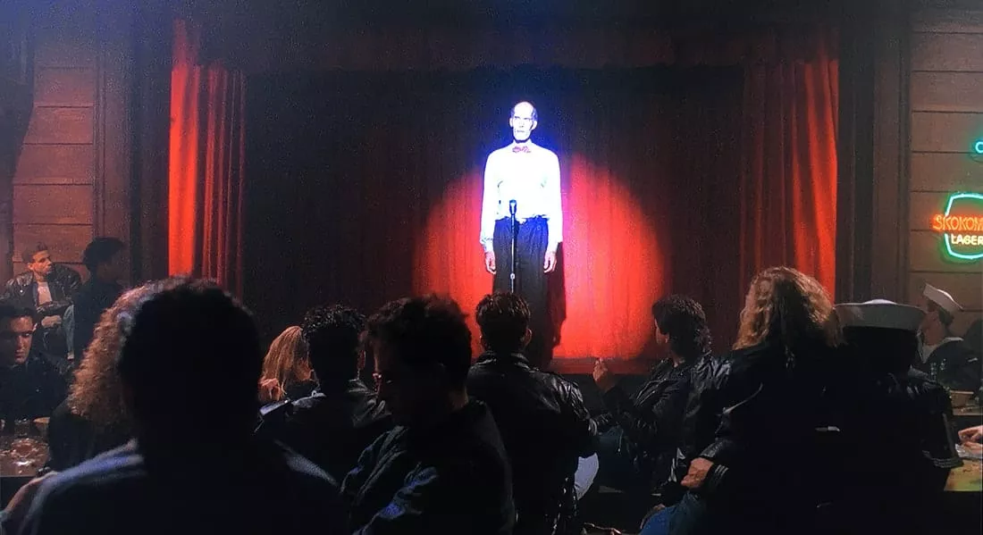 From the back of the Roadhouse you can see the tall giant on stage, in front of red curtains with a spotlight on him.