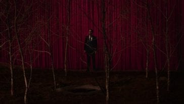 Cooper stands between a grove of sycamores and a red curtain.