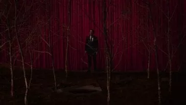 Cooper stands between a grove of sycamores and a red curtain.