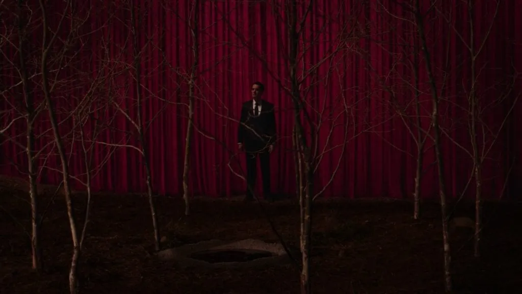 Cooper stands between a grove of sycamores and a red curtain.