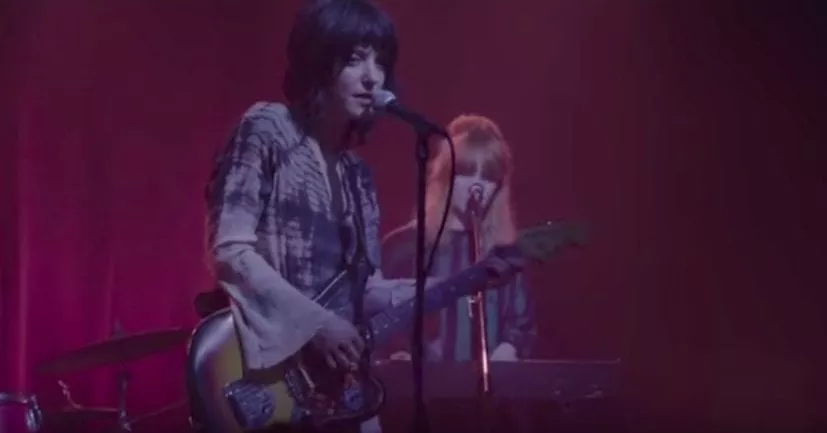 Van Etten is Centered in purple, her background singer behind her, and red curtains at the back.