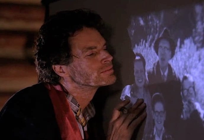 Unshaven Ben Horne leans against film projection of home videos while caressing the screen.