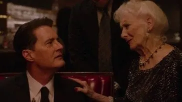 An elderly woman places her hand on the shoulder of a sitting Dale Cooper.