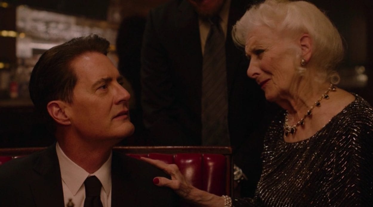 An elderly woman places her hand on the shoulder of a sitting Dale Cooper.